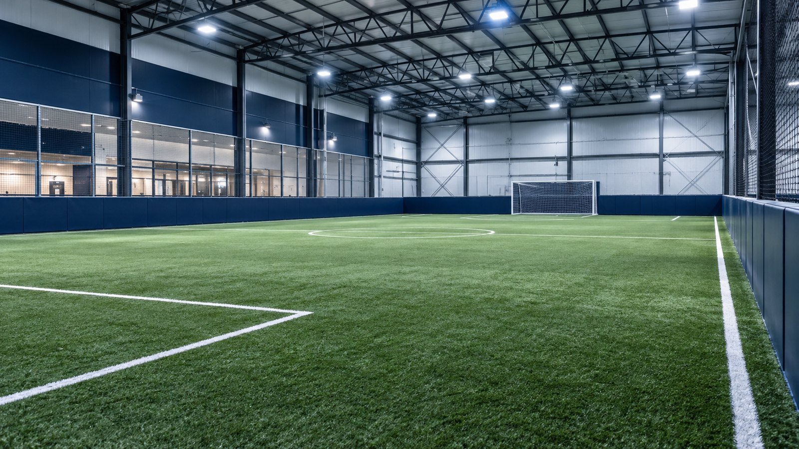 Indoor soccer field with green turf, white lines and a goal.